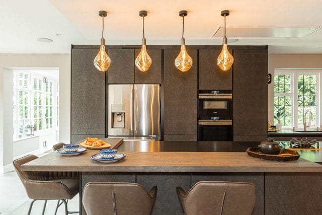 Dark textured handleless kitchen with oak island breakfast bar, amber pendant lights and integrated American fridge freezer, Ashley Jay Kitchens