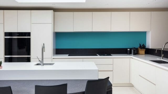 Modern white Ashley Jay kitchen with turquoise splashback, island sink and integrated ovens