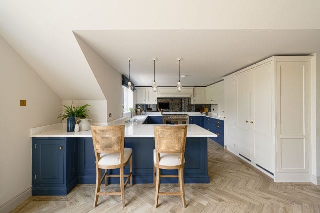 Navy blue and cream shaker kitchen with large L-shaped island, rattan bar stools and herringbone wood flooring, Ashley Jay Kitchens Horsham
