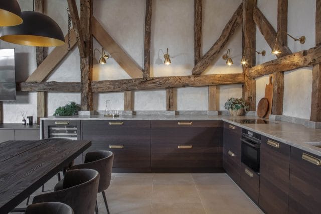 Rustic Ashley Jay kitchen with dark wood cabinetry, exposed beams, brass handles and wall lights