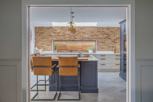 Navy blue shaker kitchen island with tan leather bar stools, exposed brick wall and skylight, Ashley Jay Kitchens