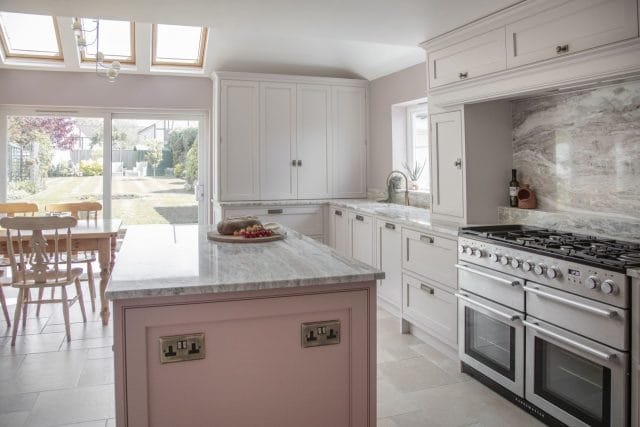 Traditional Ashley Jay kitchen with pink island, range cooker, marble-effect splashback and garden views