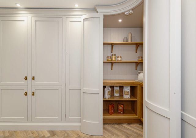 Traditional pantry cupboard with curved doors, painted cabinetry and warm wooden shelving