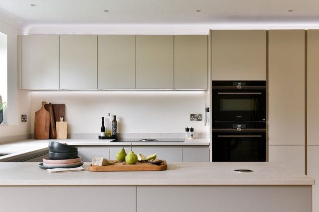 Minimal Ashley Jay kitchen with neutral cabinetry, integrated ovens, large island and under-cabinet lightin