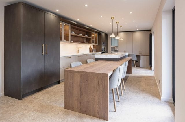 Bespoke open-plan kitchen with dark cabinetry, oak dining table, brass pendants and integrated island, Ashley Jay Kitchens