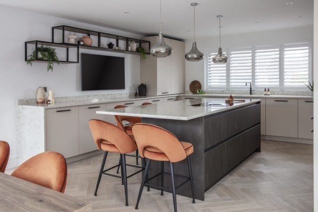 Contemporary open-plan kitchen with dark island, neutral cabinetry and orange bar stools by Ashley Jay Kitchens