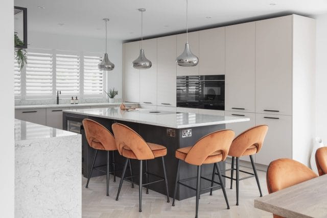 Contemporary Ashley Jay kitchen with dark island, orange bar stools, white cabinetry and pendant lighting