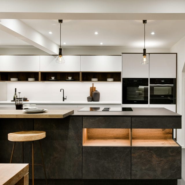 Modern Ashley Jay kitchen with dark island, white cabinetry, pendant lights and built-in ovens