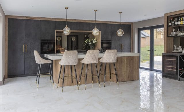 Modern Ashley Jay kitchen with dark cabinetry, wood island, pendant lights and upholstered bar stools