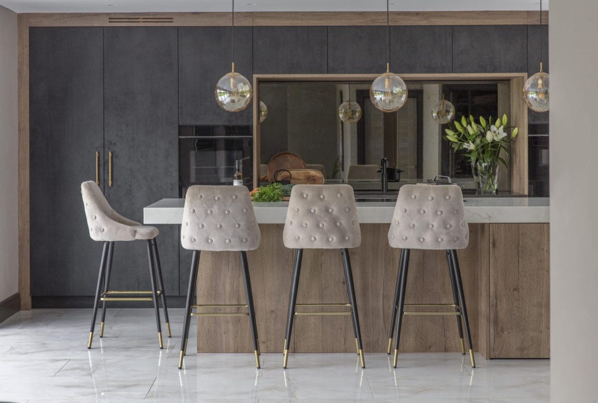 Contemporary dark kitchen with warm wood accents, a sleek waterfall island and upholstered breakfast bar stools beneath statement globe pendant lighting.