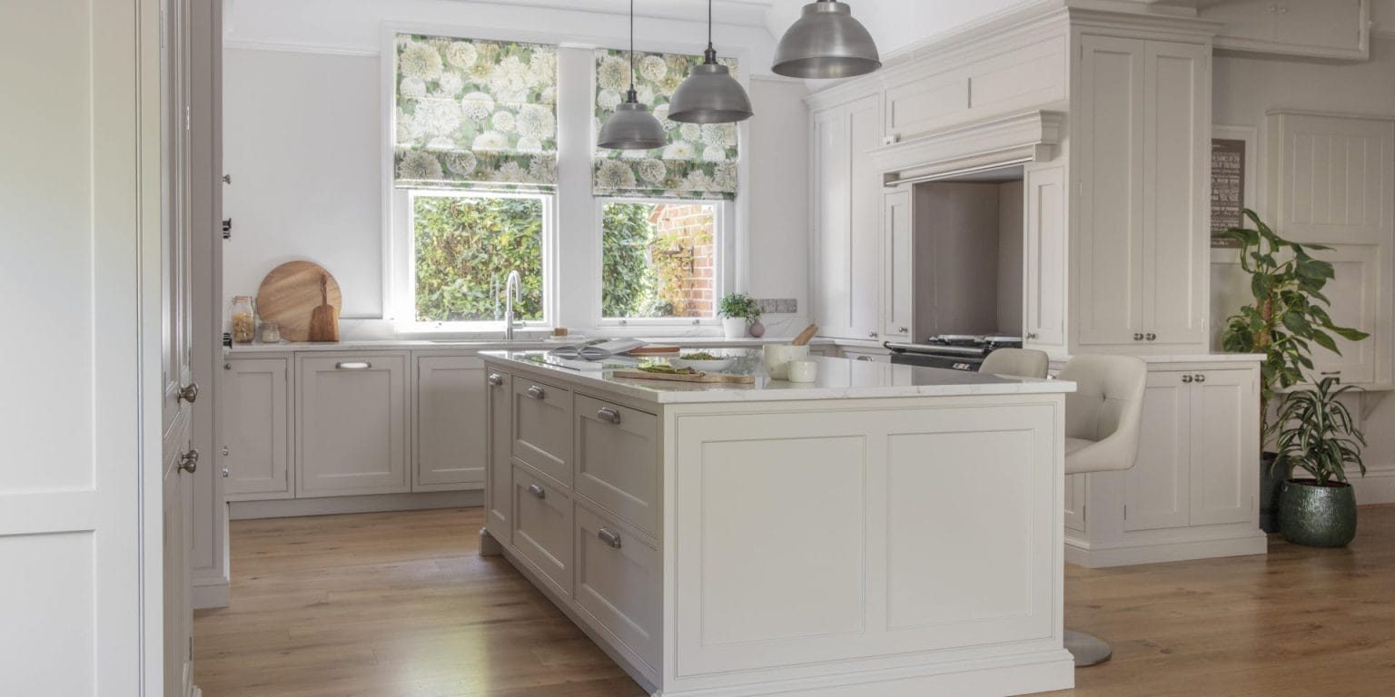 Bright, timeless shaker kitchen with a large central island, painted cabinetry, pendant lighting and floral Roman blinds creating a soft, elegant feel.